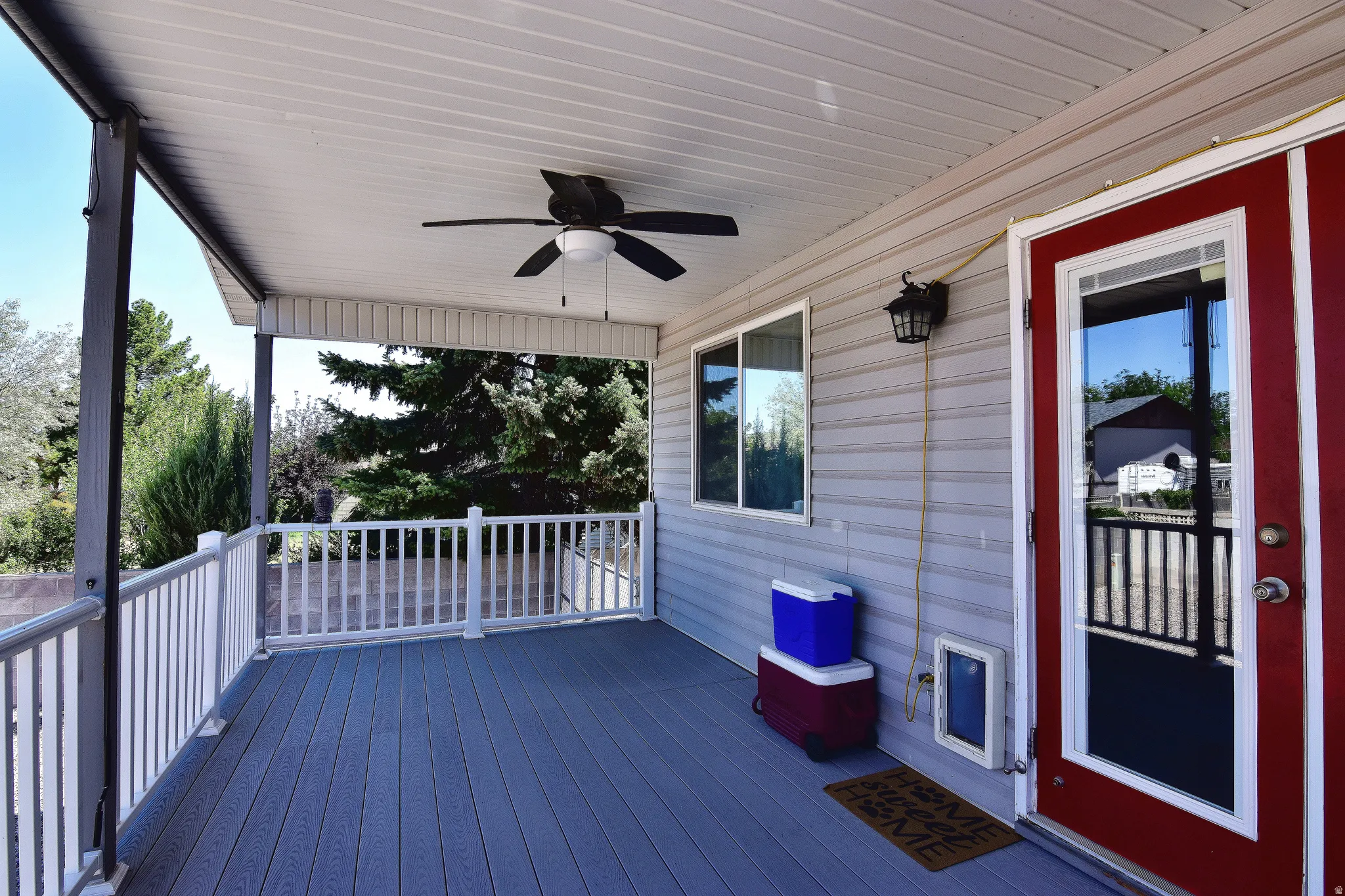 Covered porch featuring wood-finish decking, white railings, and a ceiling fan
