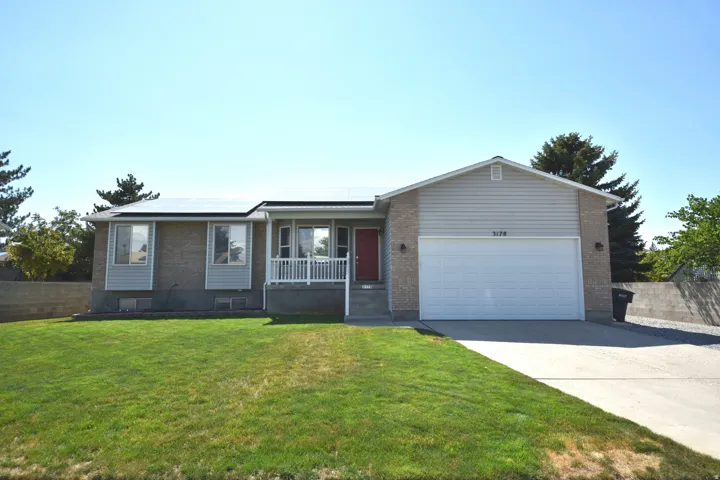 Front exterior featuring a red entry door, white porch railing, and a two-car garage