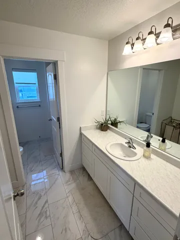 Bathroom featuring a white vanity with integrated sink, a large mirror, and a five-light fixture