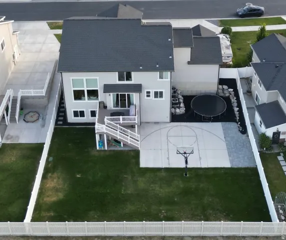 Rear exterior featuring a two-story deck with white railings, a concrete sport court, and a level lawn