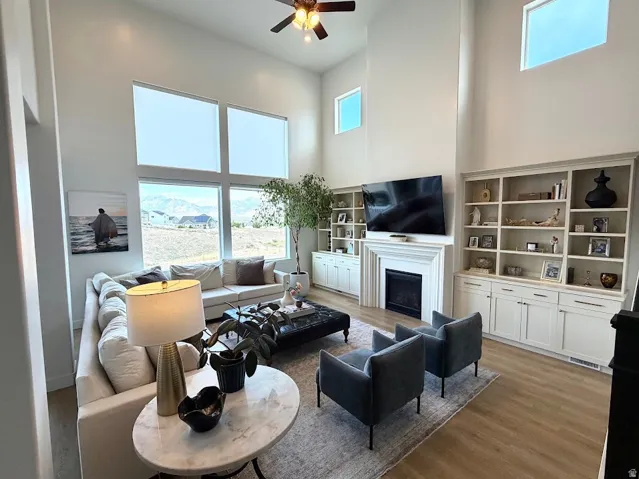 Great room featuring soaring ceilings, expansive window walls, a fireplace with a detailed mantel, custom built-in shelving, and wood-finish flooring
