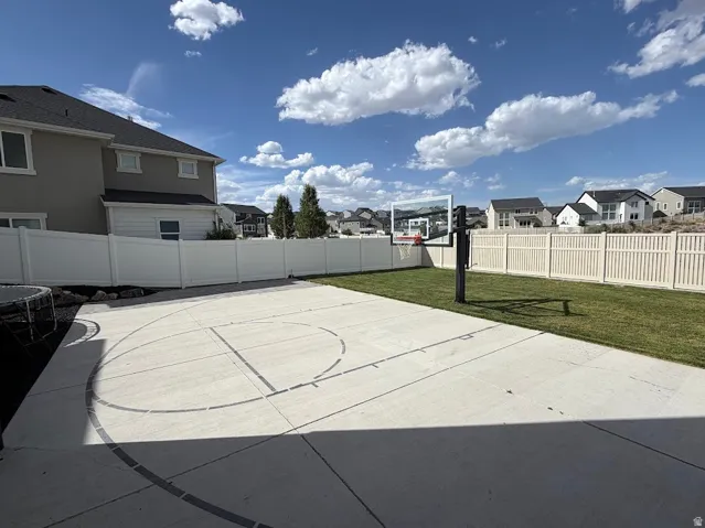 Expansive backyard featuring a concrete sport court with painted lines, a manicured lawn, and a white privacy fully fenced backyard.