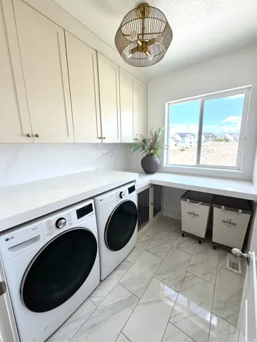 Laundry room featuring marble-look tile flooring, extensive white cabinetry with gold-toned hardware, white solid surface countertops, and a built-in window desk