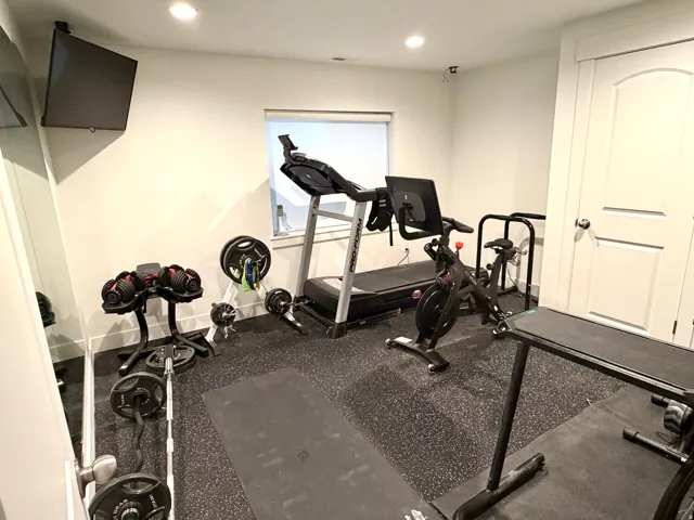 Dedicated fitness space featuring resilient black flooring, a wall-mounted television, and recessed ceiling lighting