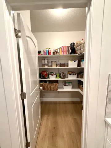 Walk-in pantry featuring light wood-finish flooring, white shelving, recessed lighting, and a paneled door