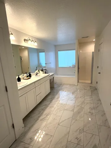 Spacious bathroom featuring a dual vanity with white cabinetry, a large built-in mirror, a soaking tub, and a separate glass-enclosed shower