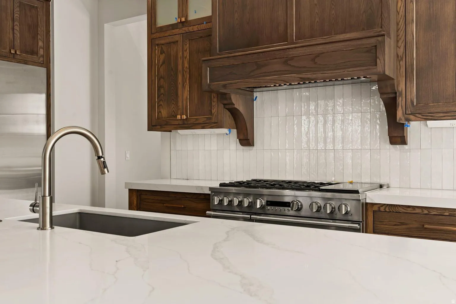 Kitchen featuring white countertops, an undermount sink with a gooseneck faucet, a stainless steel range, and wood cabinetry with a custom range hood