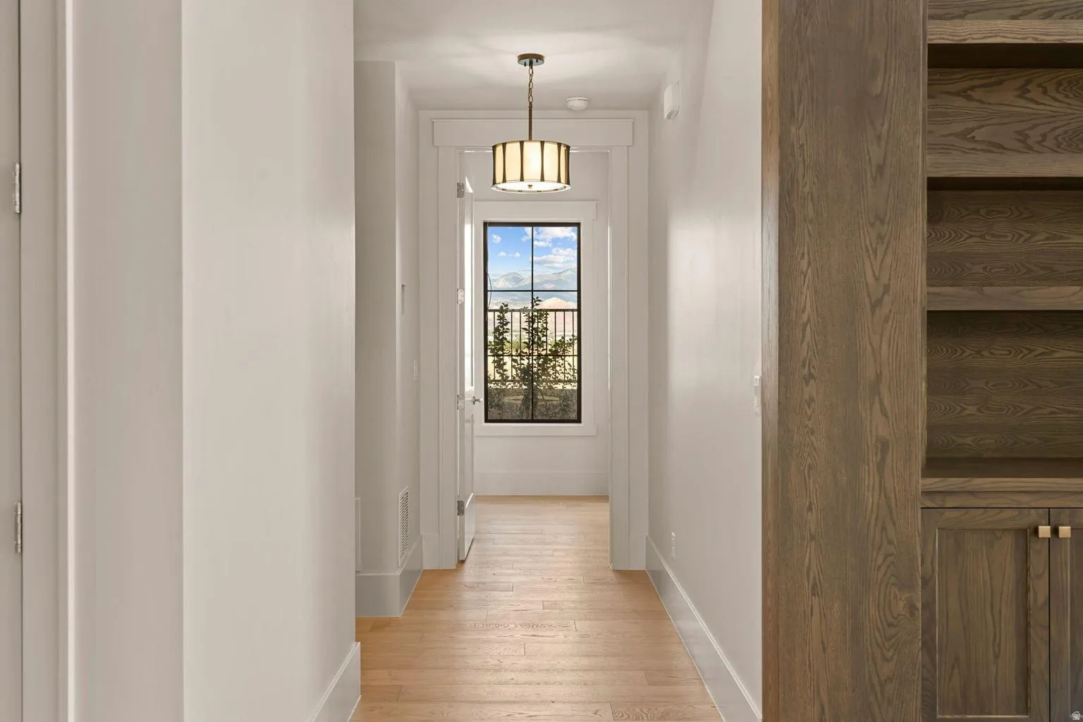 Hallway featuring light wood-finish flooring, white walls, and a large window with black grilles