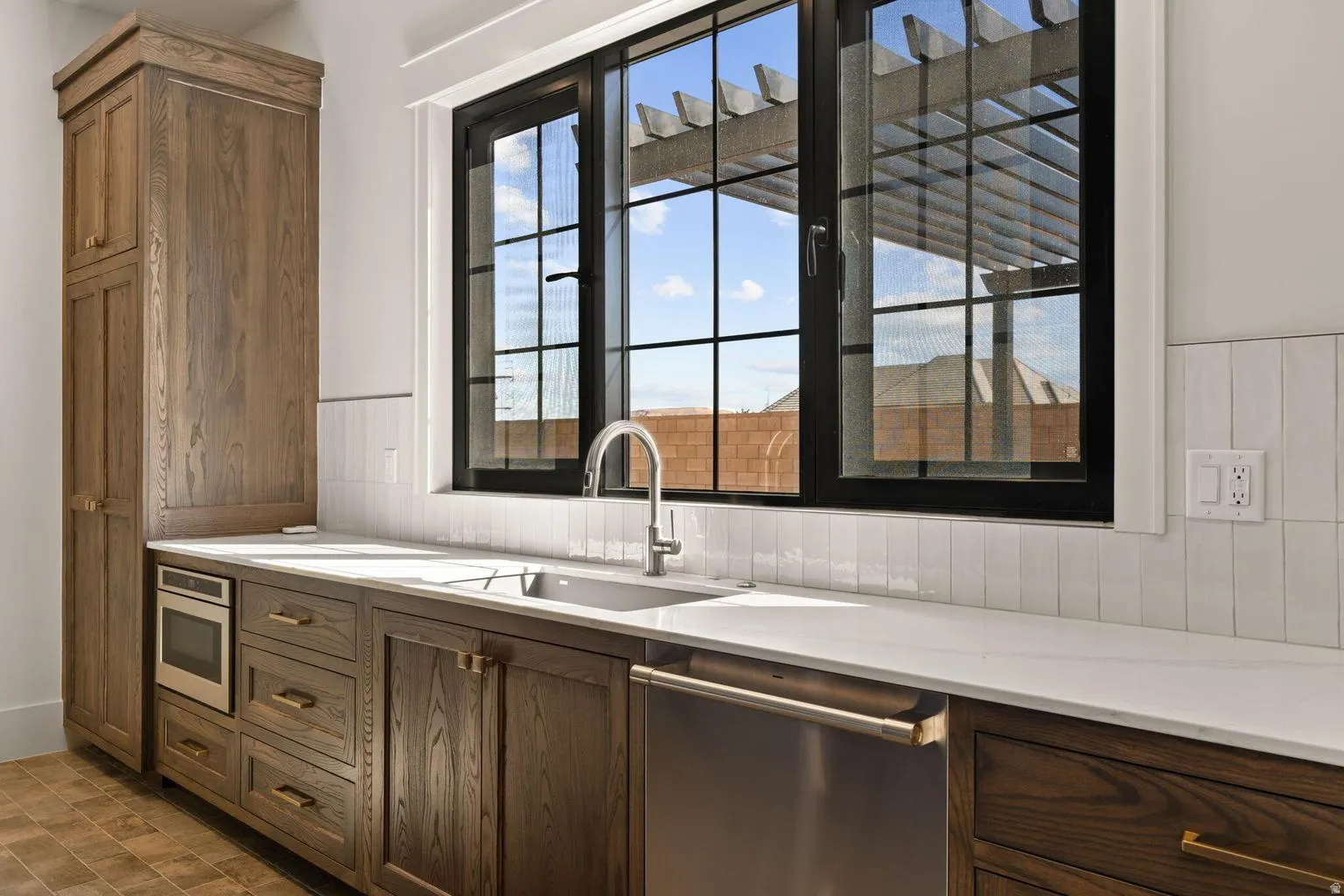 Kitchen area featuring a prominent black-framed window, white subway tile backsplash, and light-colored countertops