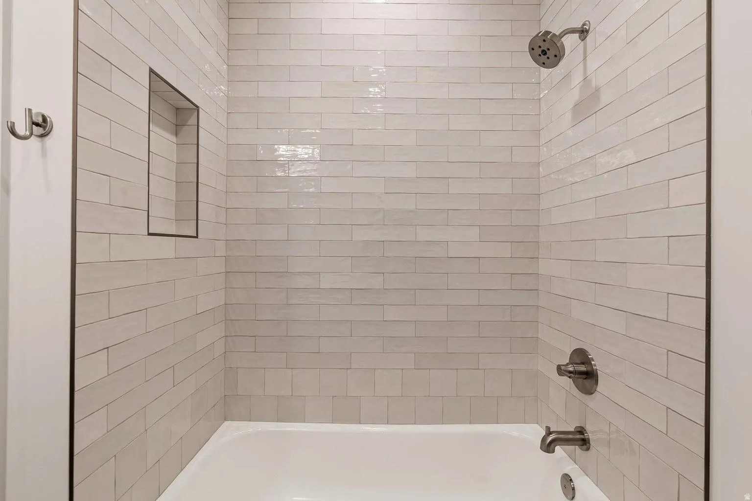Bathtub with subway tile surround, recessed shower niche, and brushed nickel fixtures