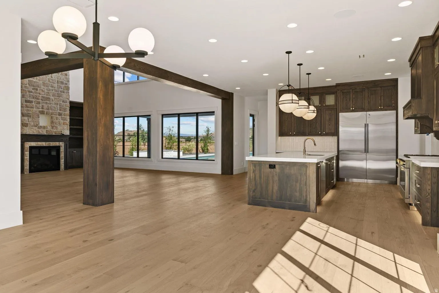 Open-concept living space featuring wood-finish flooring, a stone-faced fireplace, a vaulted ceiling with exposed wood beams, and large windows