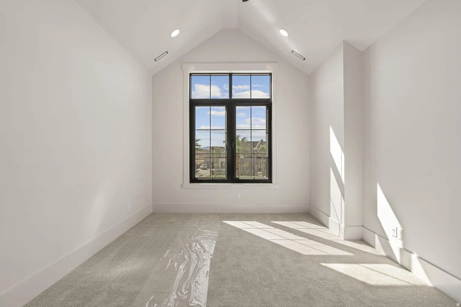 Vaulted ceiling with recessed lighting and a large black-framed window