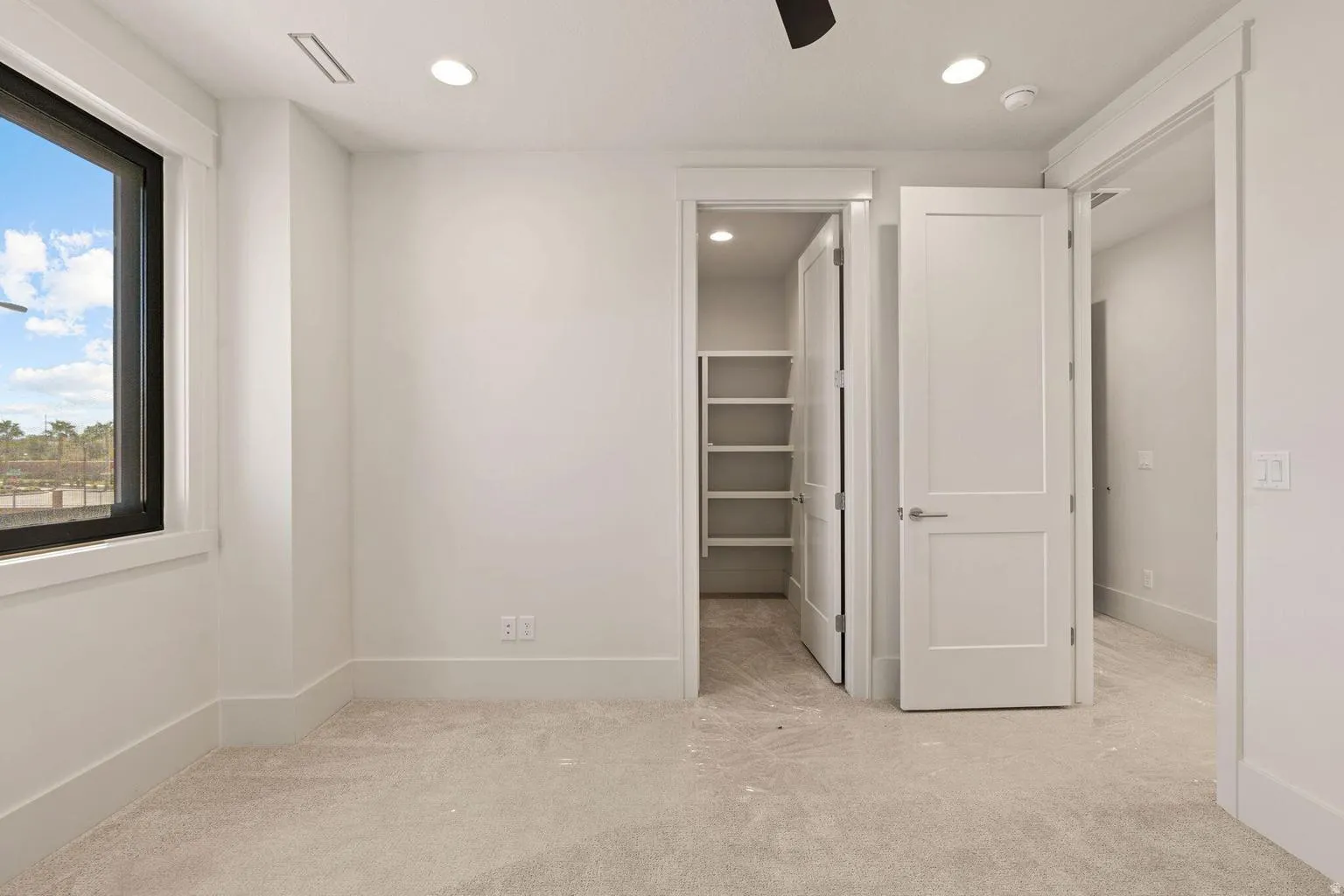 Carpeted room featuring a large window with black trim, recessed lighting, white baseboards, and a walk-in closet with built-in shelving