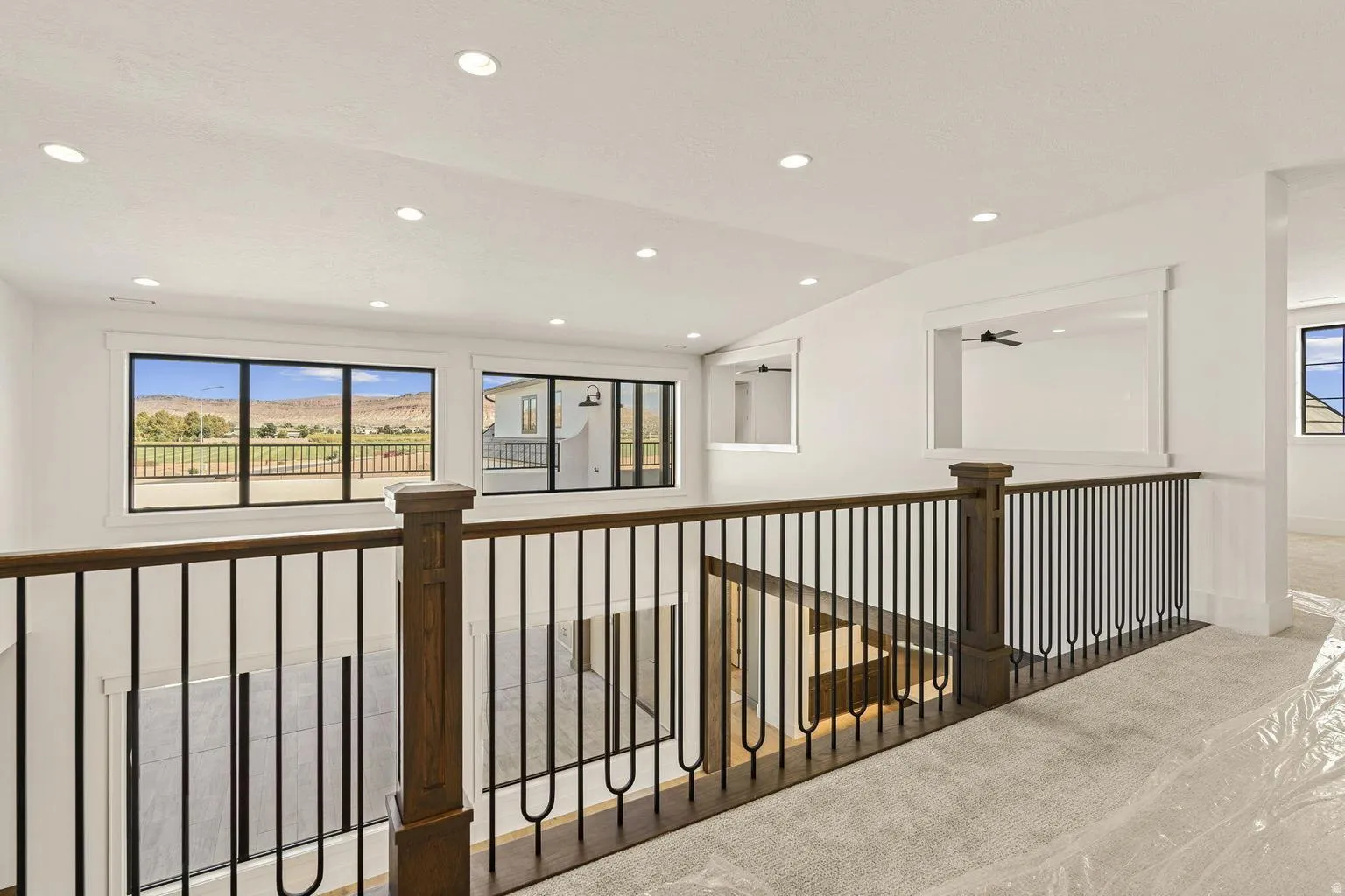 Upper-level landing featuring a wood-finish and wrought iron railing, recessed lighting, expansive windows with mountain scenery, and light-toned carpeting