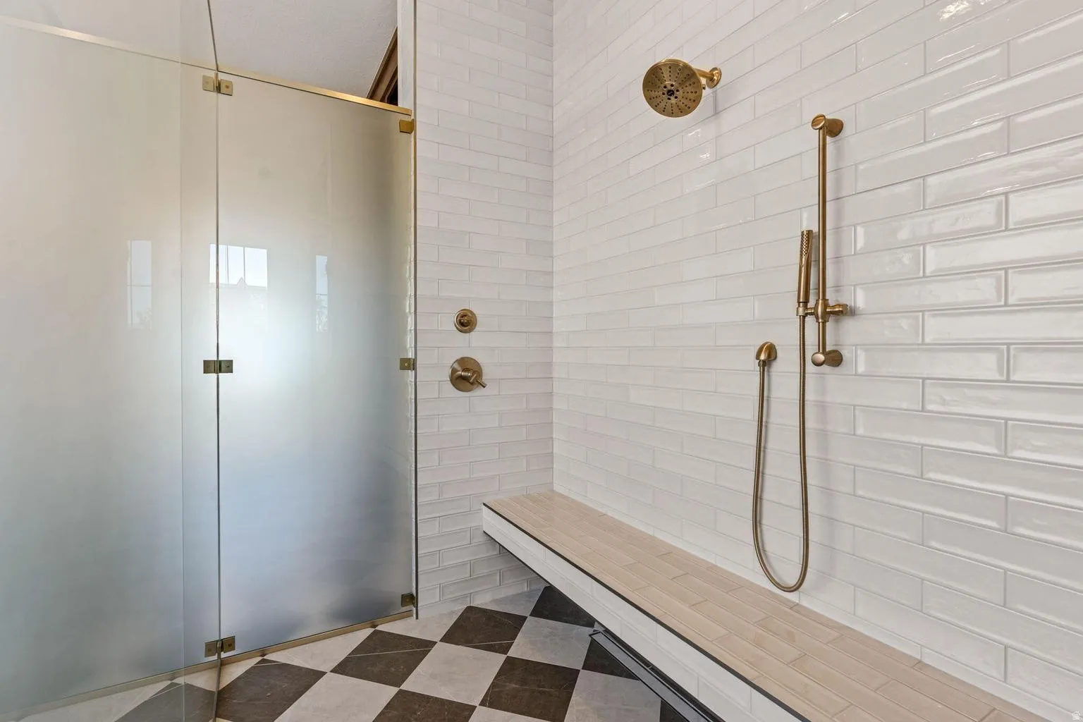 Walk-in shower with frosted glass enclosure, bronze-finish fixtures, white subway tile walls, built-in bench, and checkerboard floor tiling