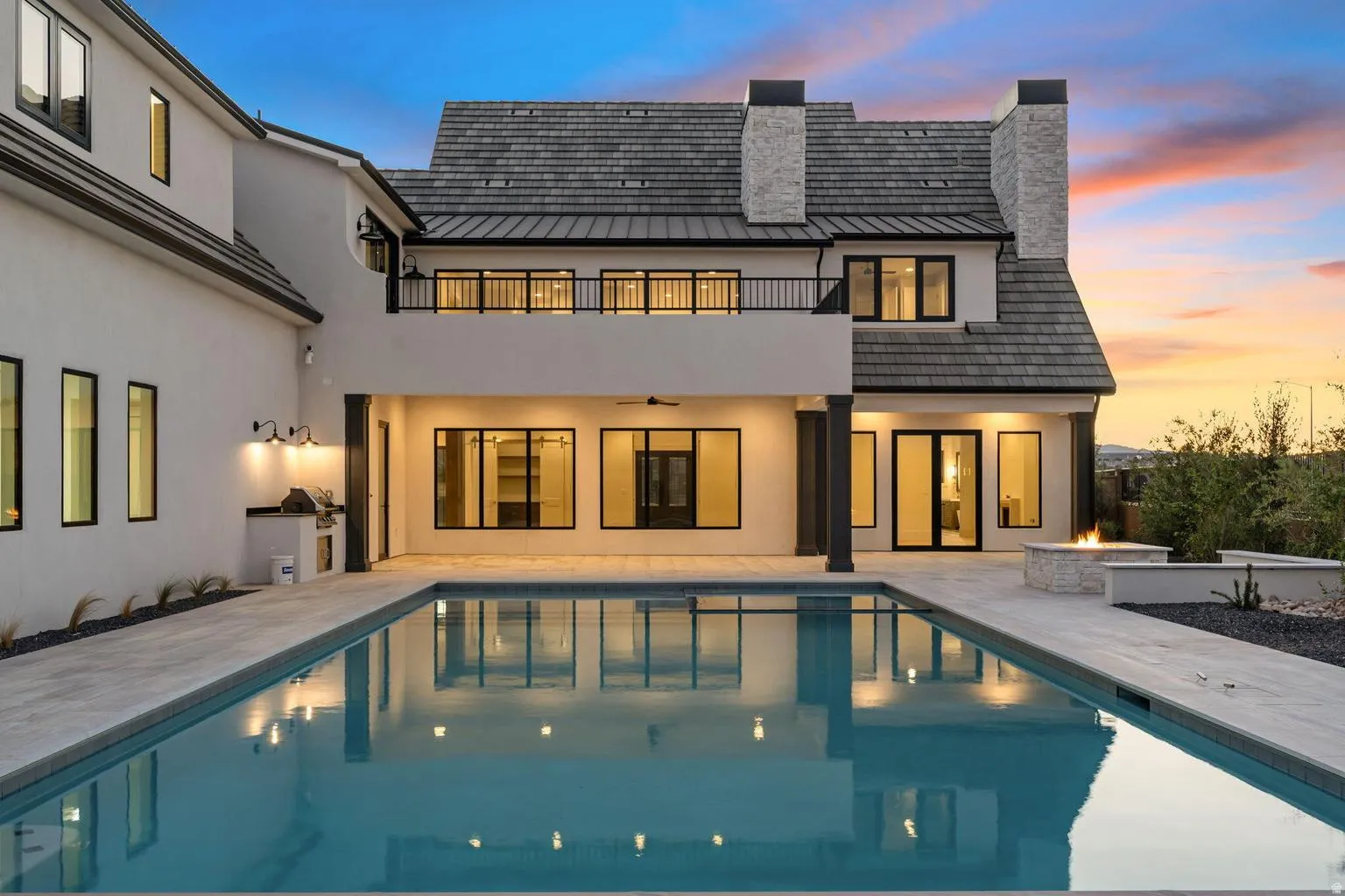 Expansive backyard oasis featuring a rectangular swimming pool, a built-in outdoor kitchen, an outdoor fire feature, and a second-story balcony