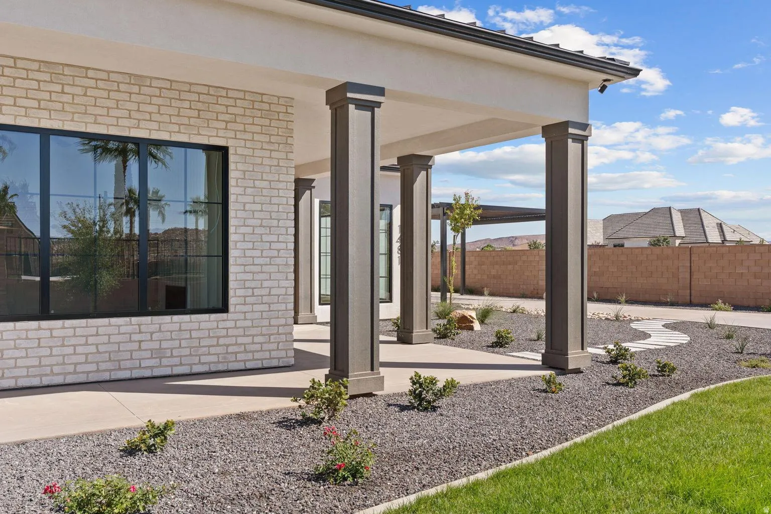 Exterior patio featuring robust columns, light-toned brick facade, and large black-framed windows