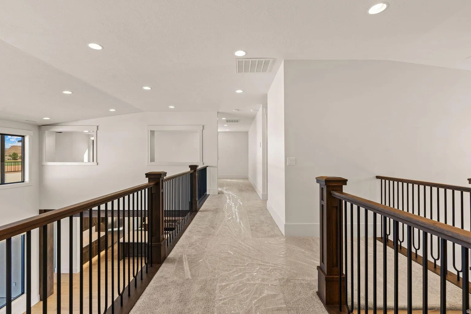 Upper-level hallway featuring recessed lighting, a carpeted floor, and dark wood railings with black iron balusters