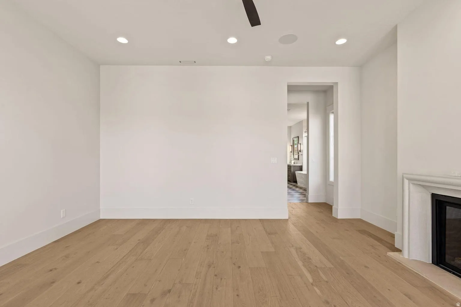 Spacious room featuring light wood-finish flooring, recessed lighting, a ceiling fan, and a built-in fireplace with a stone mantel