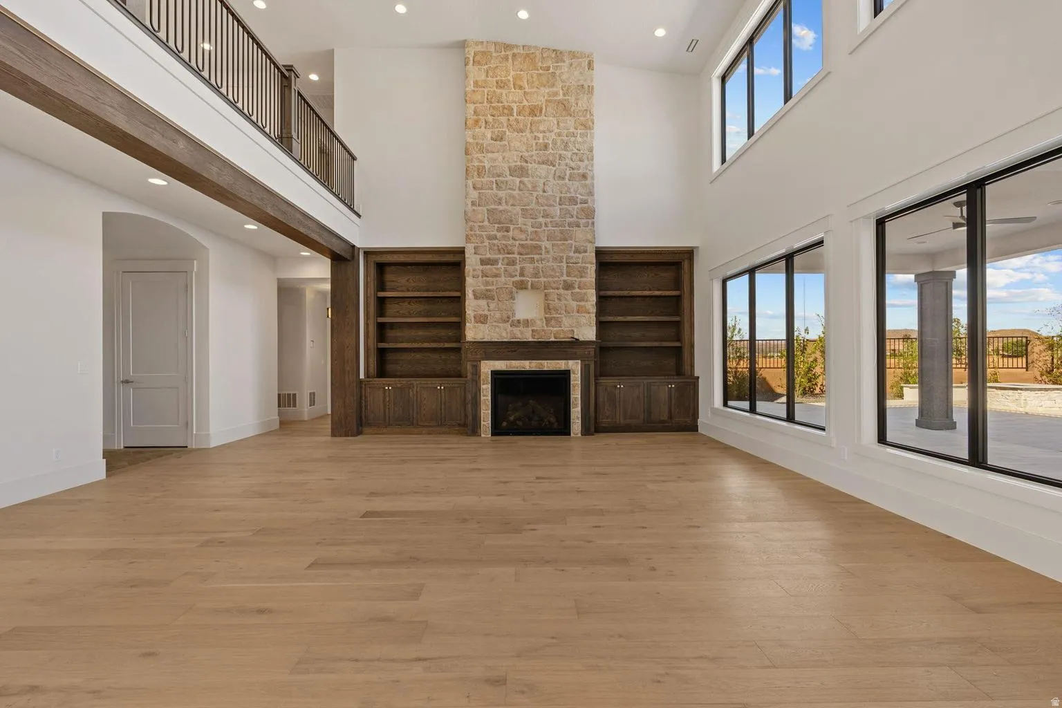 Spacious interior featuring a stone fireplace, built-in shelving, high ceilings, wood-finish flooring, and expansive windows