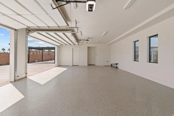 Spacious garage featuring a light-colored epoxy floor, multiple windows, a roll-up garage door, and recessed lighting