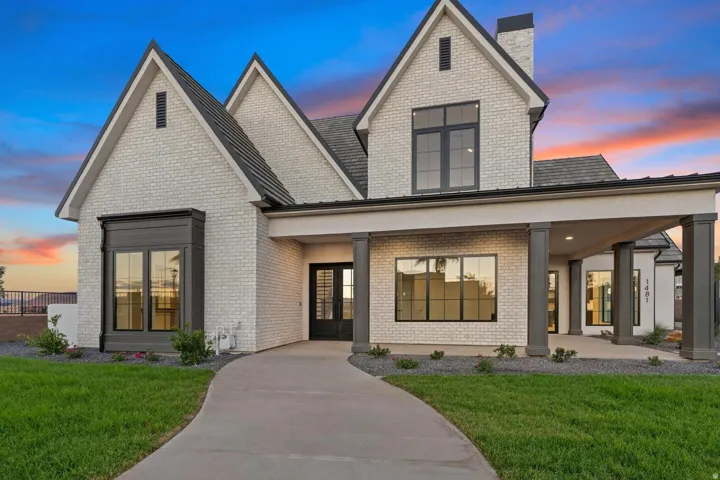 Modern farmhouse architectural style featuring white brick exterior, dark-framed windows, contrasting gables, a covered entry with dark columns, and a landscaped front yard with a curved concrete path