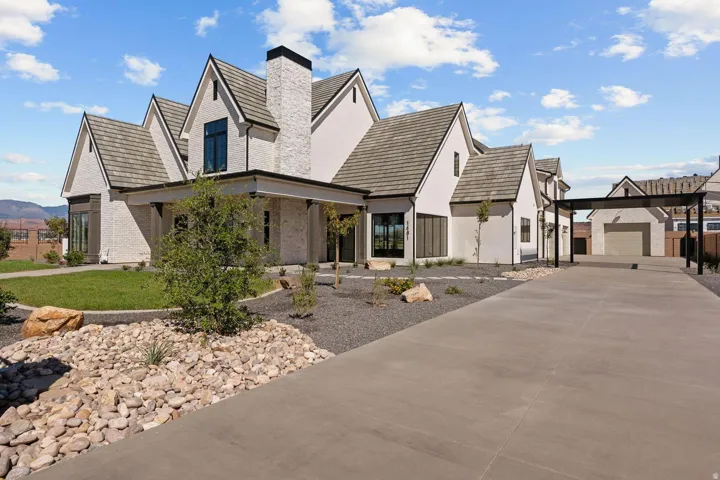 Contemporary white stucco exterior with multiple gables, a prominent chimney, dark-framed windows, and an extensive concrete driveway leading to a detached garage