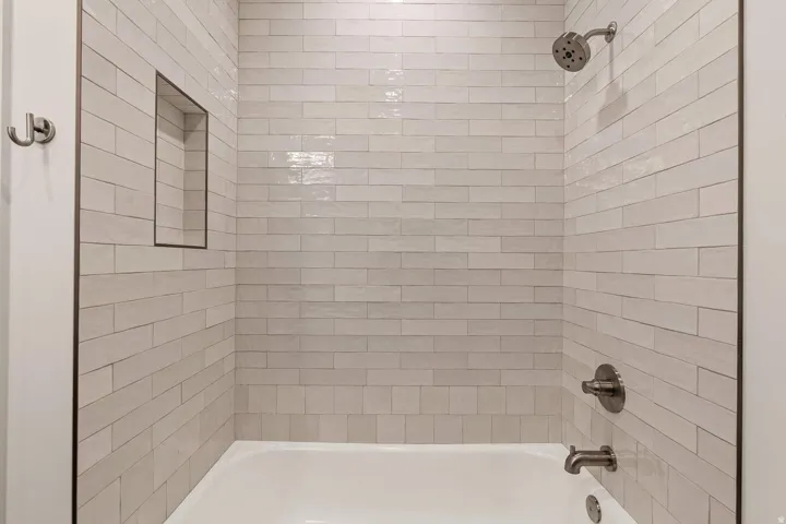 Bathtub with subway tile surround, recessed shower niche, and brushed nickel fixtures