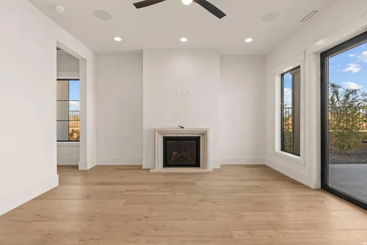Bright interior space featuring light wood-finish flooring, a fireplace with a stone surround, recessed lighting, and a ceiling fan