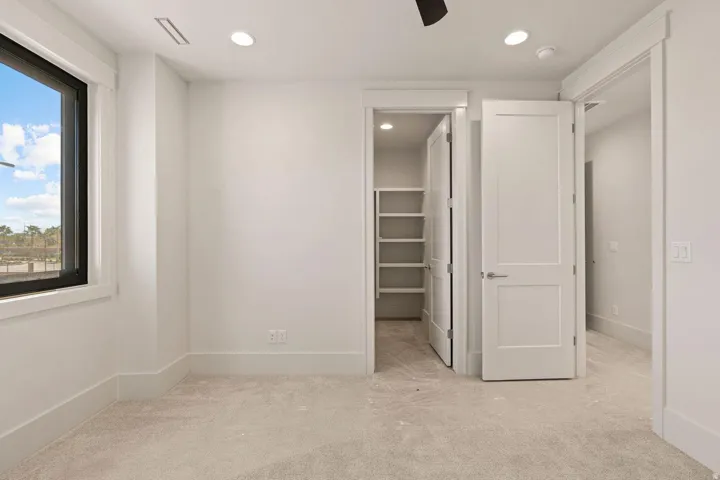 Carpeted room featuring a large window with black trim, recessed lighting, white baseboards, and a walk-in closet with built-in shelving