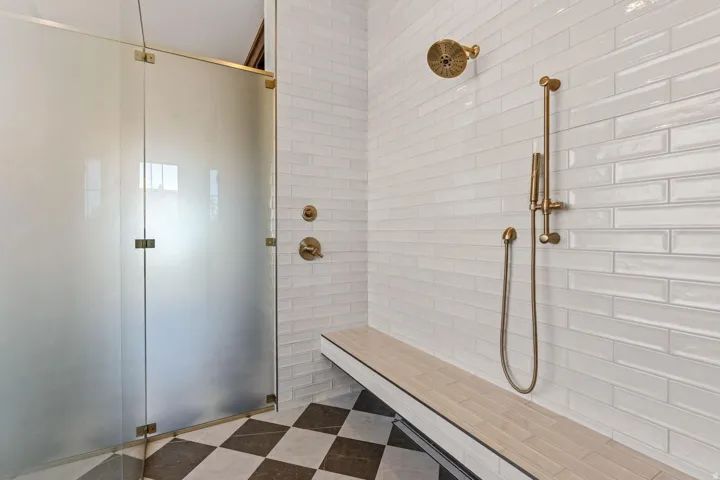 Walk-in shower with frosted glass enclosure, bronze-finish fixtures, white subway tile walls, built-in bench, and checkerboard floor tiling