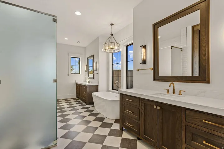 Bathroom featuring a freestanding tub, dual wood-finish vanities with countertop sinks, a checkered tile floor, and a frosted glass shower enclosure