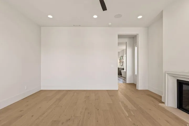 Spacious room featuring light wood-finish flooring, recessed lighting, a ceiling fan, and a built-in fireplace with a stone mantel