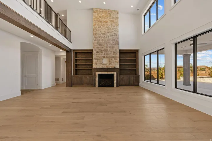 Spacious interior featuring a stone fireplace, built-in shelving, high ceilings, wood-finish flooring, and expansive windows