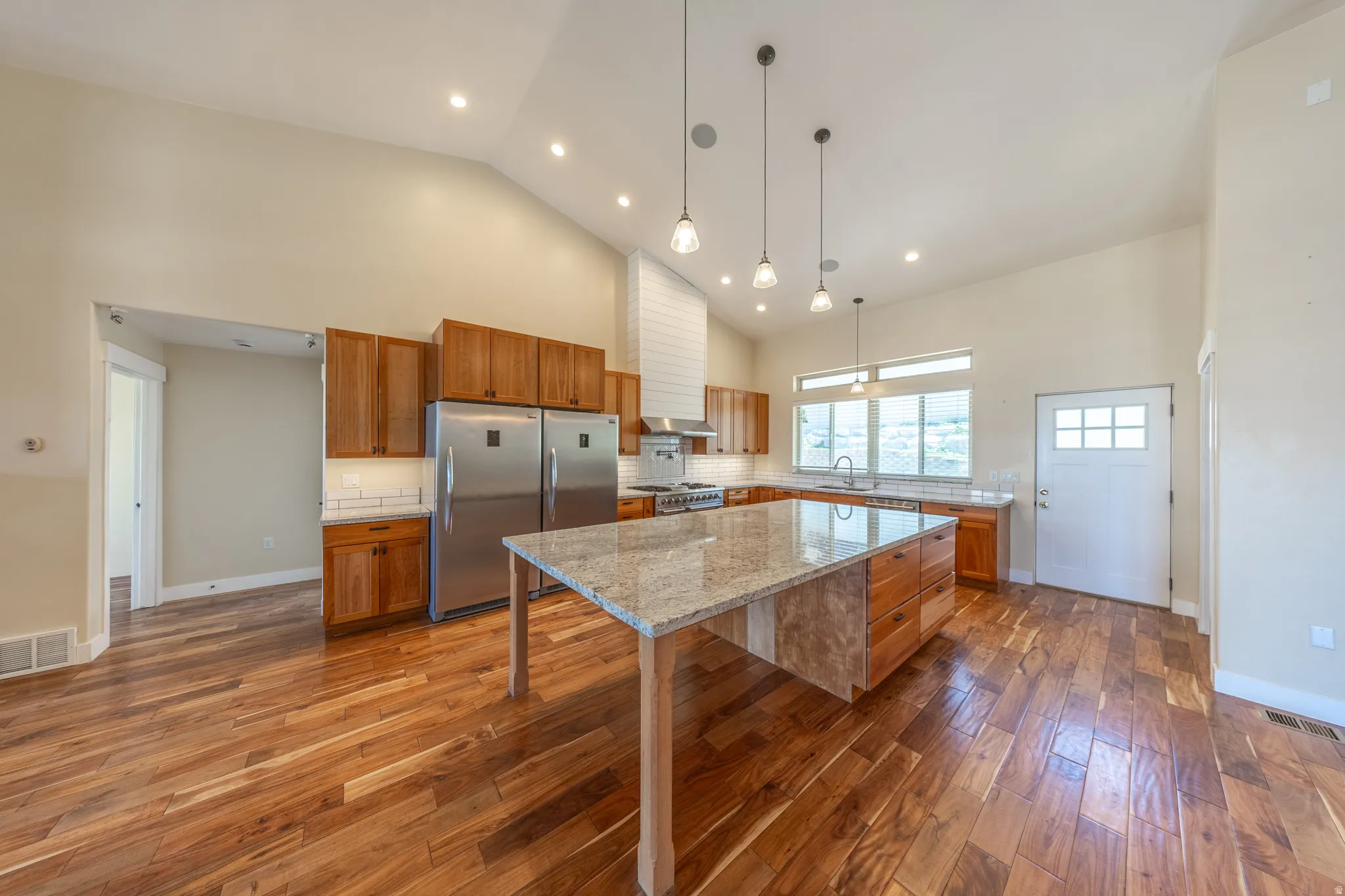 Vaulted ceilings enhance this kitchen featuring a spacious island with granite countertop, coordinating wood cabinetry, stainless steel appliances, and wood-finish flooring