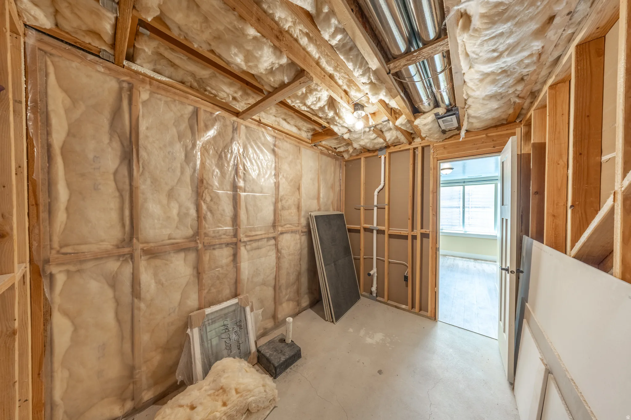 Framed interior space featuring exposed insulation, wood ceiling beams, and concrete flooring