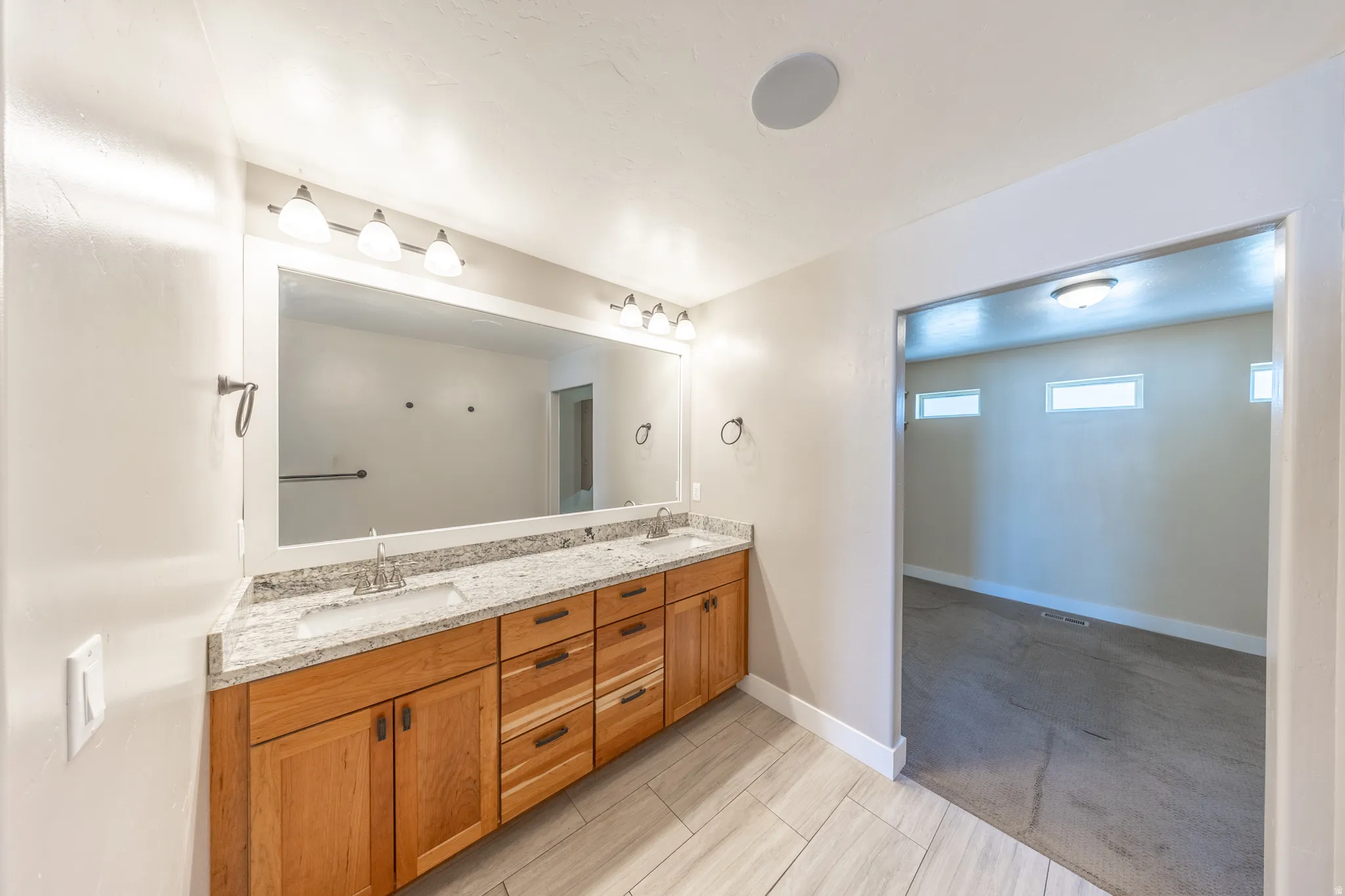 Primary suite bath features a dual vanity with wood cabinetry, granite countertop, and undermount sinks
