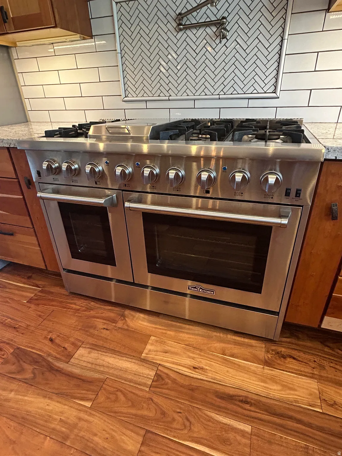 Stainless steel professional-grade range with double ovens, a six-burner gas cooktop, 15,000 BTU flat top skillet and a pot filler faucet mounted on backsplash.