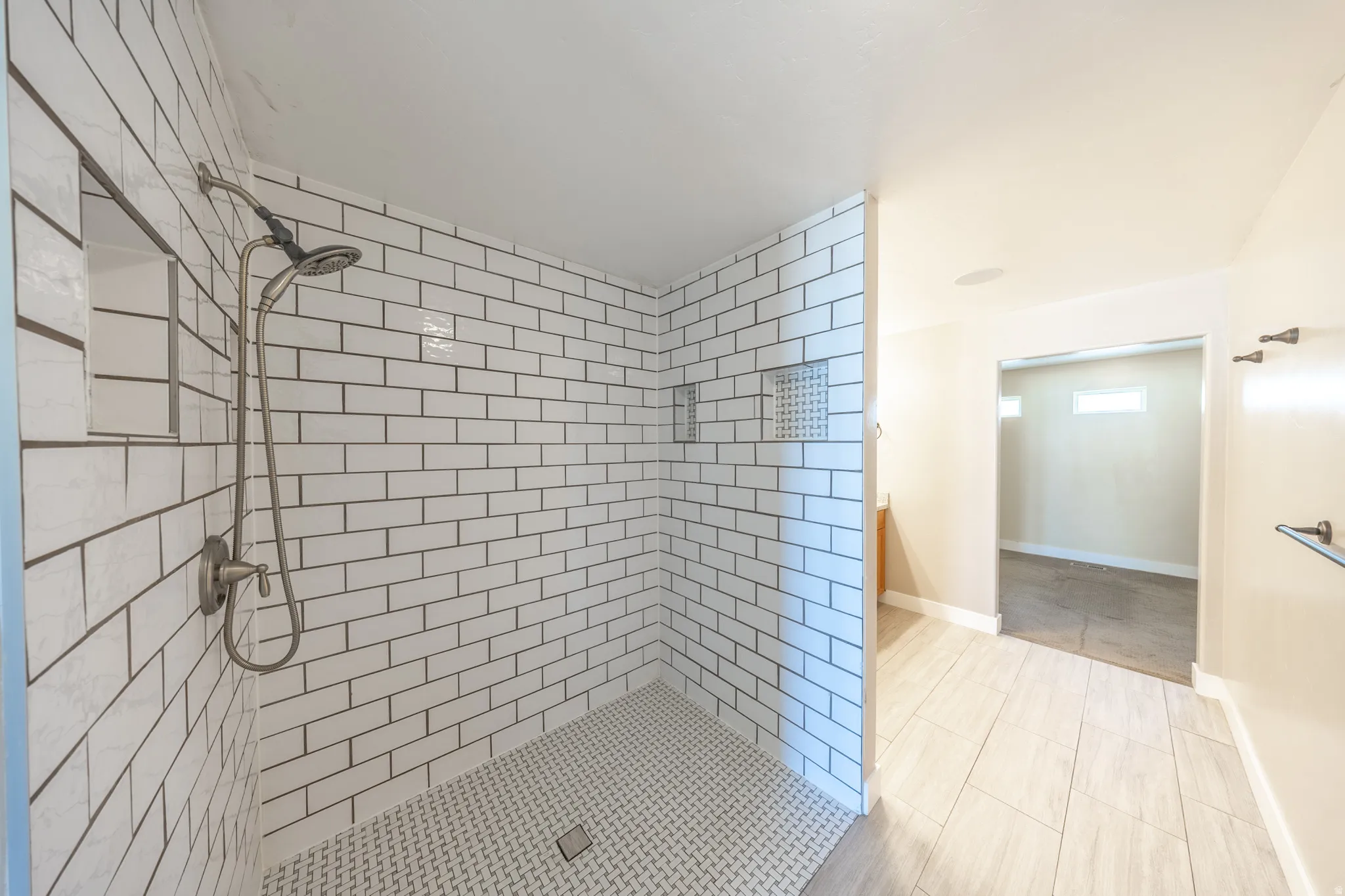 Primary suite walk-in shower with white subway tile walls and a mosaic tile floor