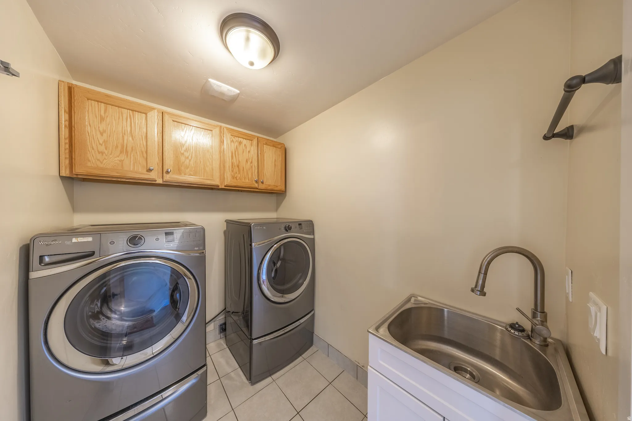 Main floor laundry is adjacent to mud room. Laundry area featuring wood-finish cabinetry, a utility sink with a gooseneck faucet, and white square tile flooring. Washer & dryer included.