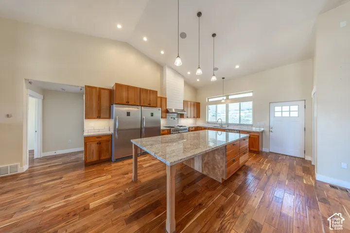 Vaulted ceilings enhance this kitchen featuring a spacious island with granite countertop, coordinating wood cabinetry, stainless steel appliances, and wood-finish flooring