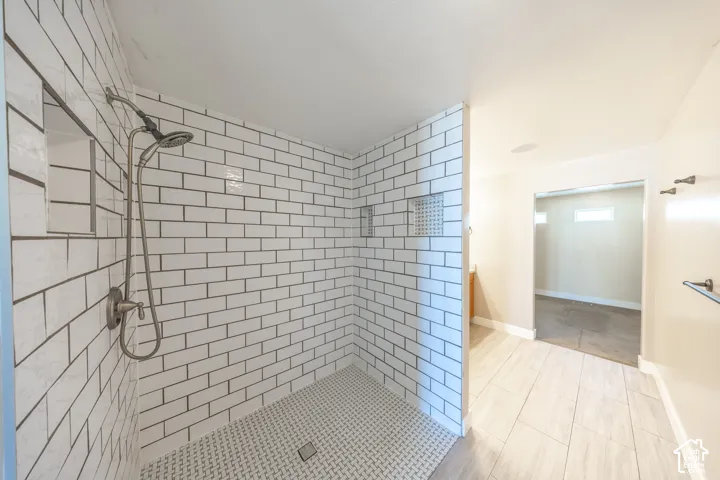 Primary suite walk-in shower with white subway tile walls and a mosaic tile floor