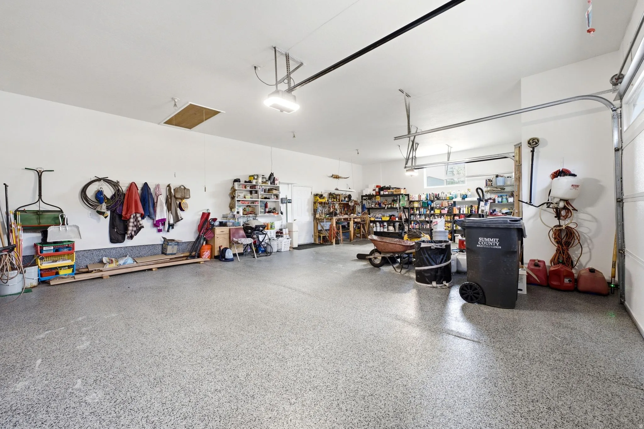 Spacious garage featuring a durable speckled epoxy floor, multiple overhead light fixtures, exposed garage door tracks, and an attic access panel