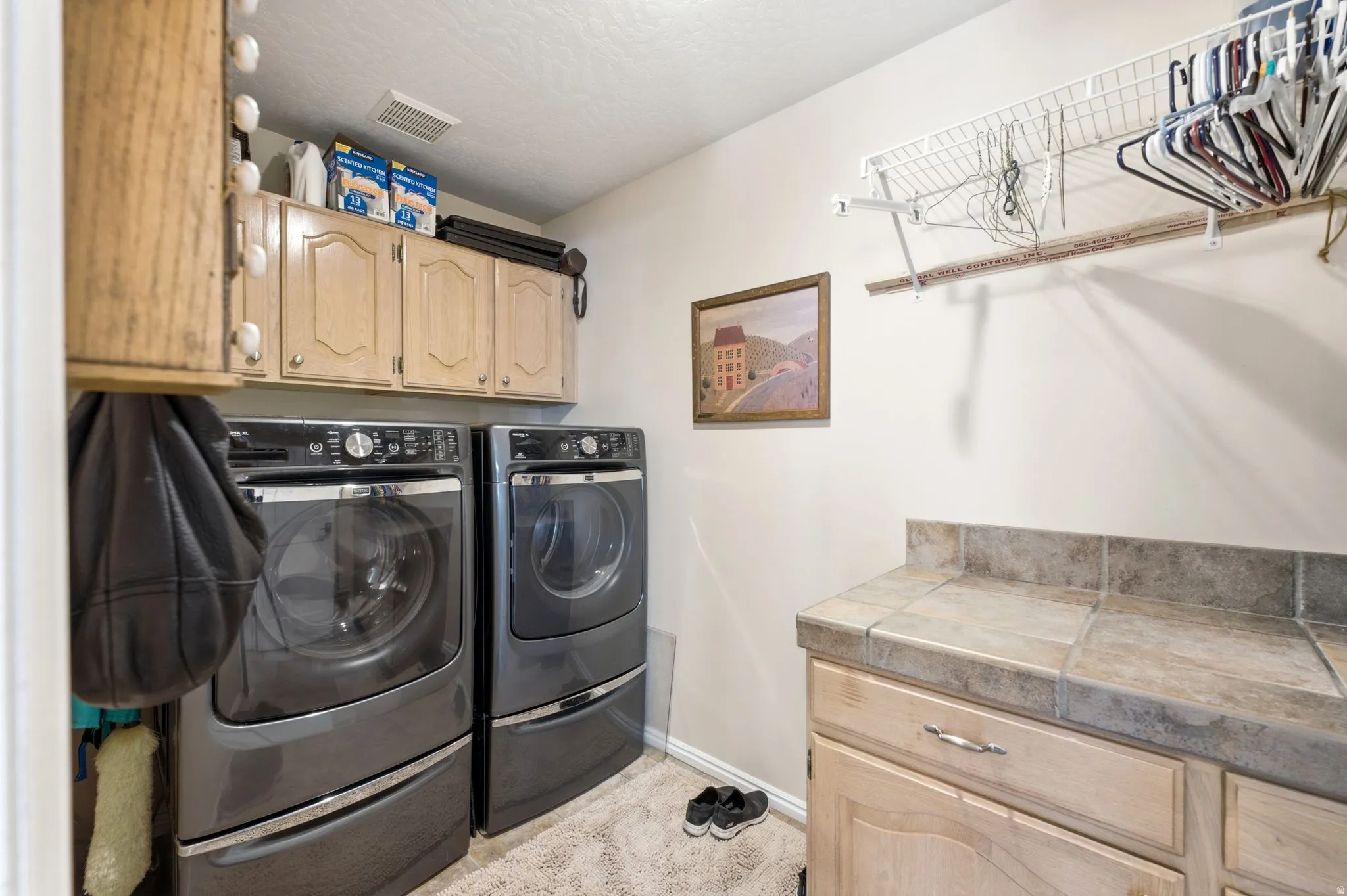Dedicated laundry room featuring built-in cabinetry, tile countertops, and a wire shelving system