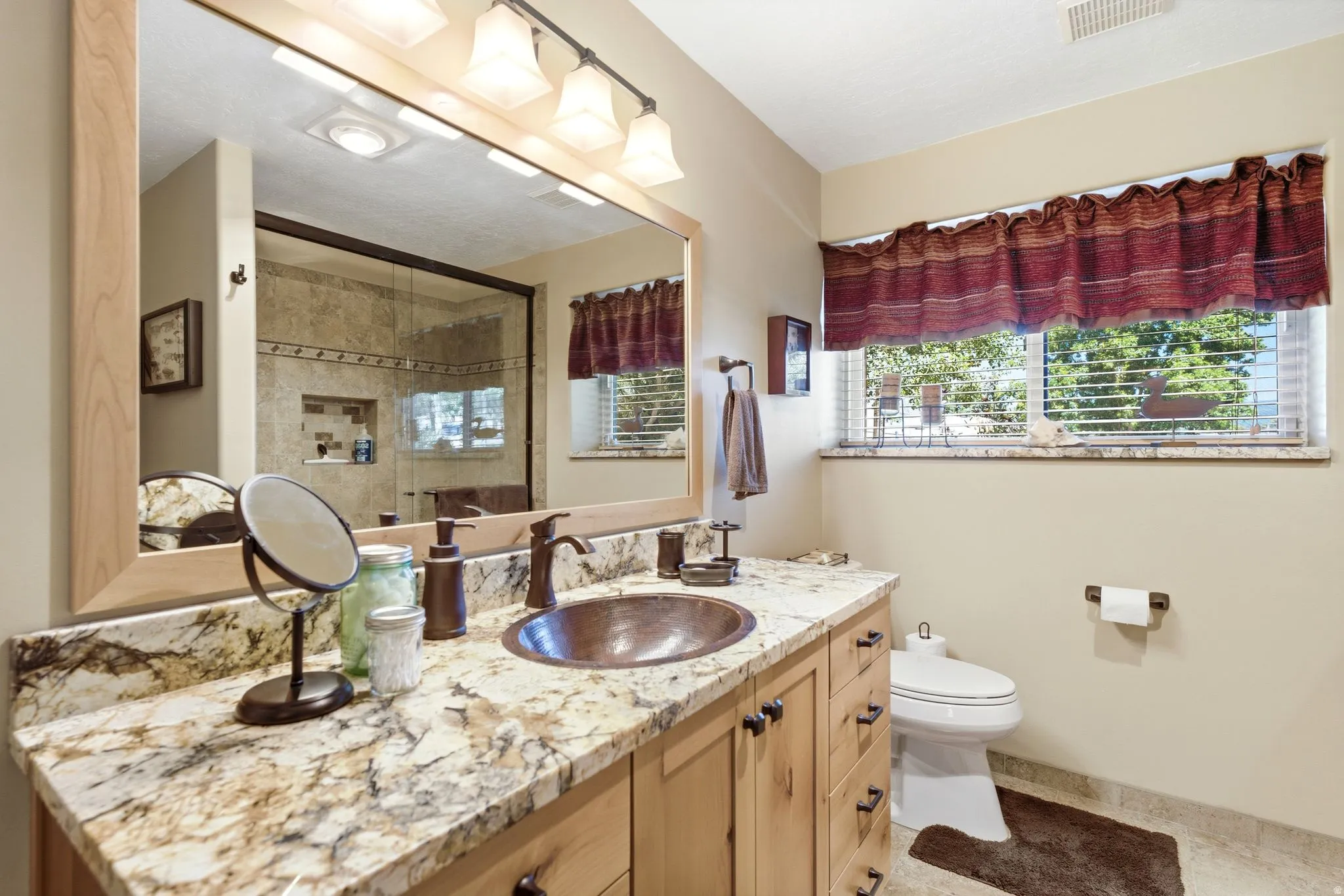 lower level Bathroom suite vanity featuring a copper basin sink, stone countertop, wood-finish cabinetry, and framed mirror with integrated lighting