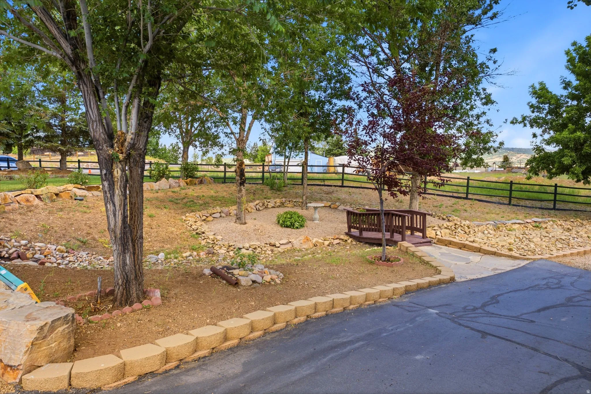 Landscaped yard featuring mature trees, a decorative footbridge, and natural stone retaining walls