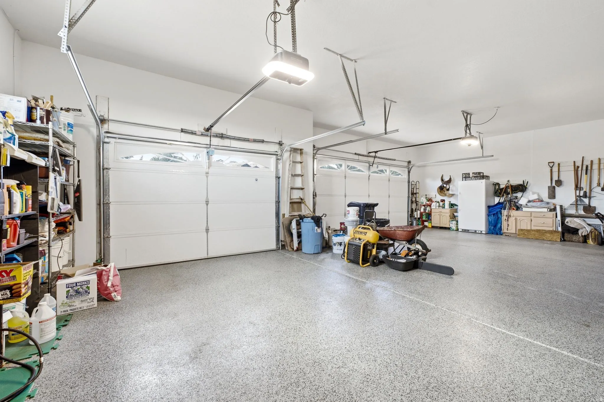 Spacious garage featuring a durable epoxy-coated concrete floor, two overhead garage doors with window inserts, and overhead lighting