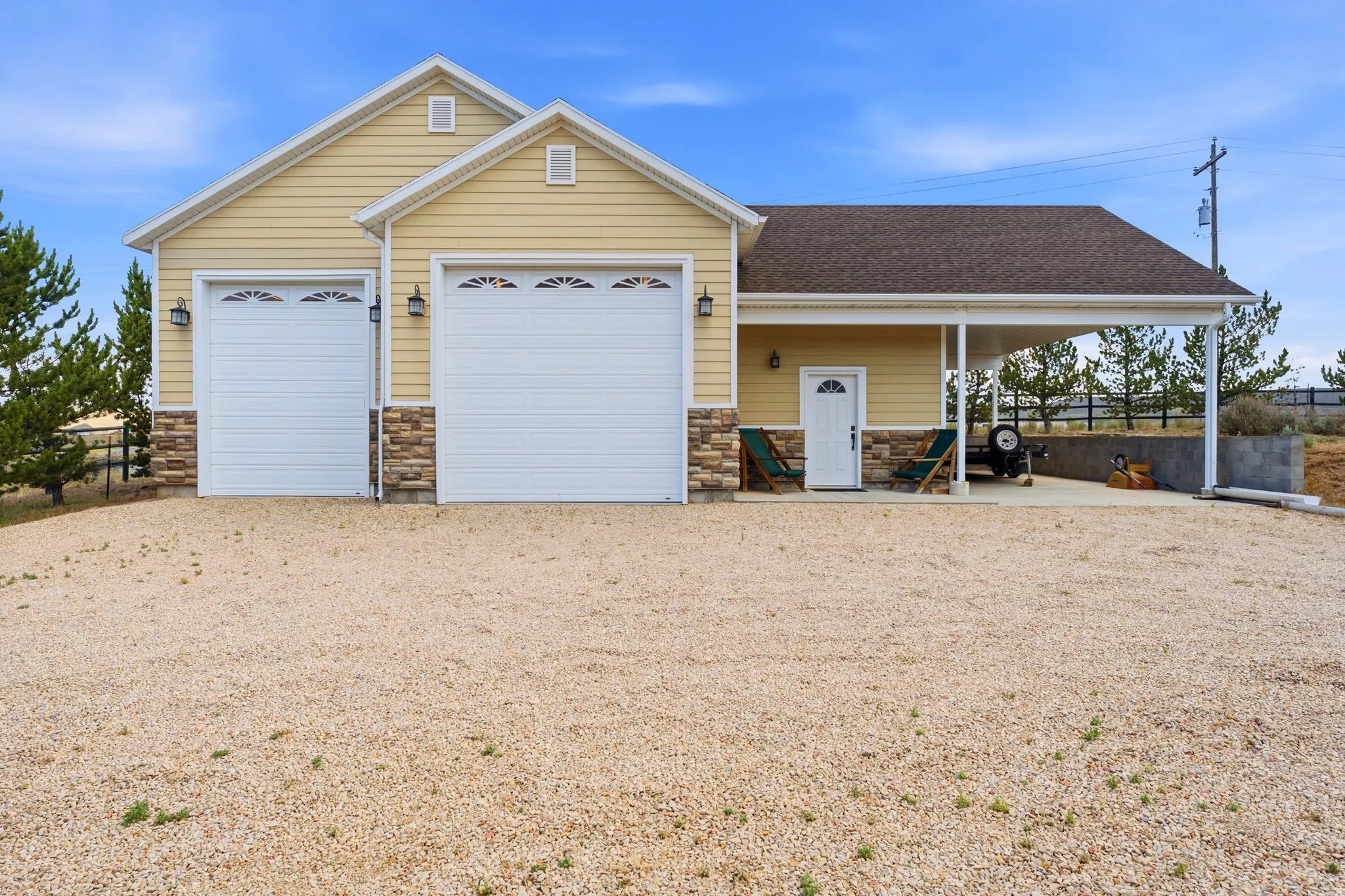 Yellow cement board siding exterior featuring two garage bays with decorative glass inserts, stone veneer accents, a covered carport, and a separate entry door