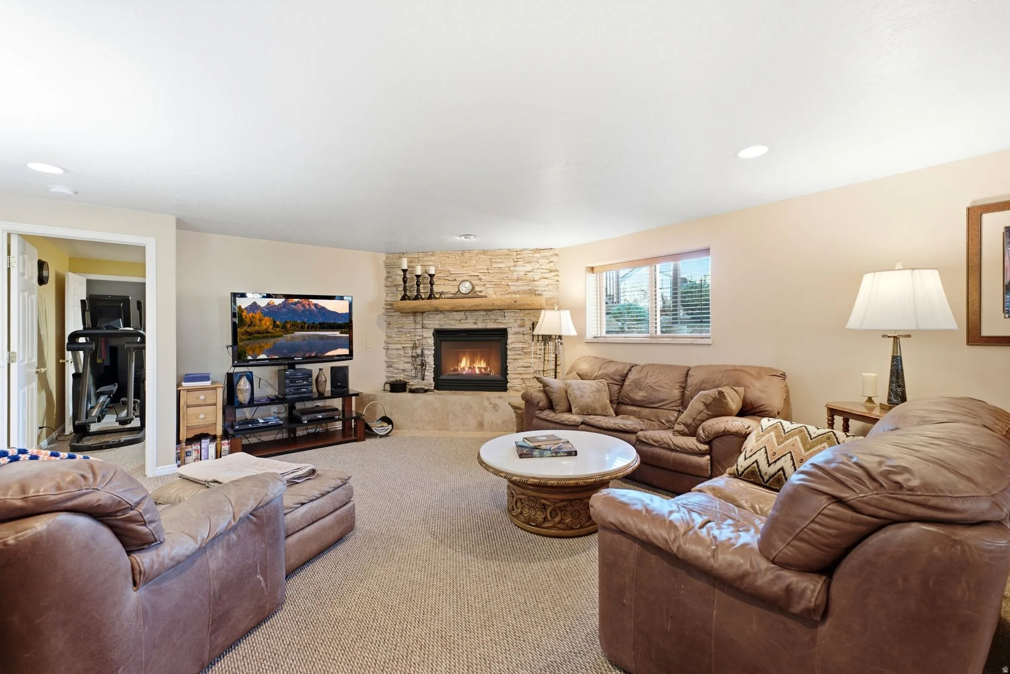 Spacious lower level living area featuring a stacked stone fireplace with a natural wood mantle, recessed lighting, and soft neutral wall tones