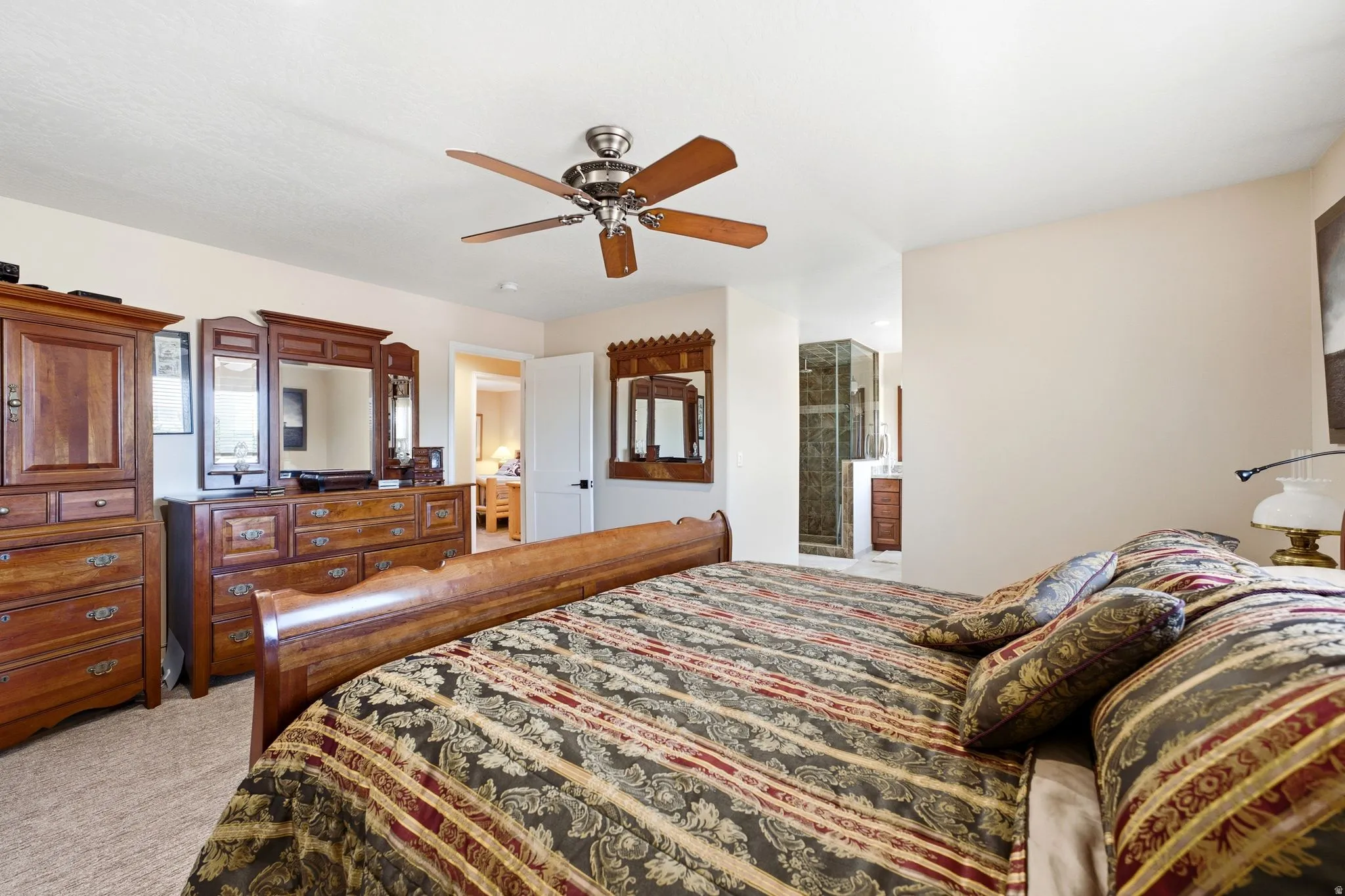 Spacious primary bedroom featuring light-toned wall paint, carpet flooring, and a ceiling fan with wood-finish blades